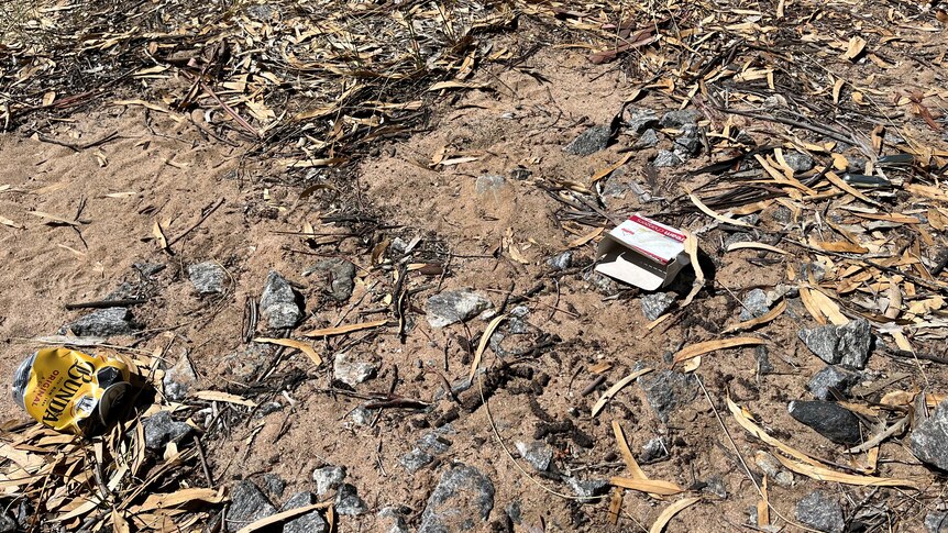 a crushed rum can with silver capsules littered in the dirt