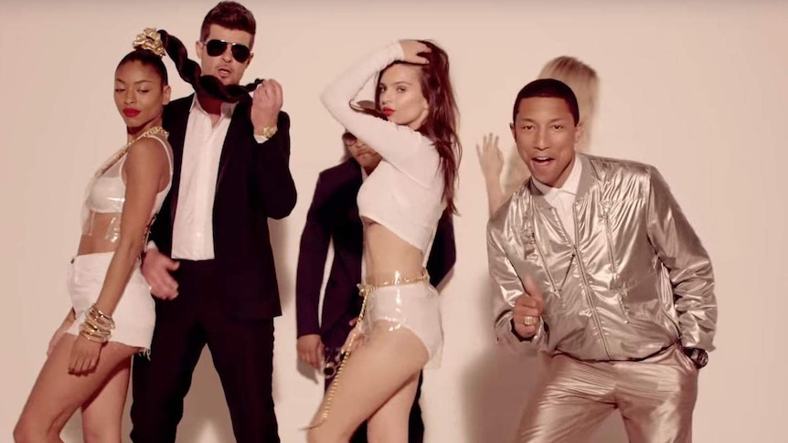 Robin Thicke and Pharrell Williams wearing suits with three women wearing revealing clothing in the film clip for Blurred Lines