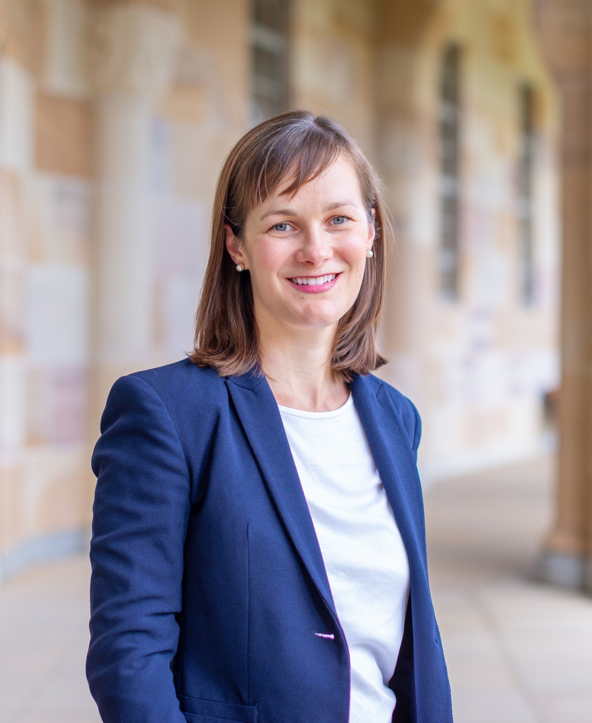 Mulher de blusa branca e terno azul em frente a um prédio de arenito