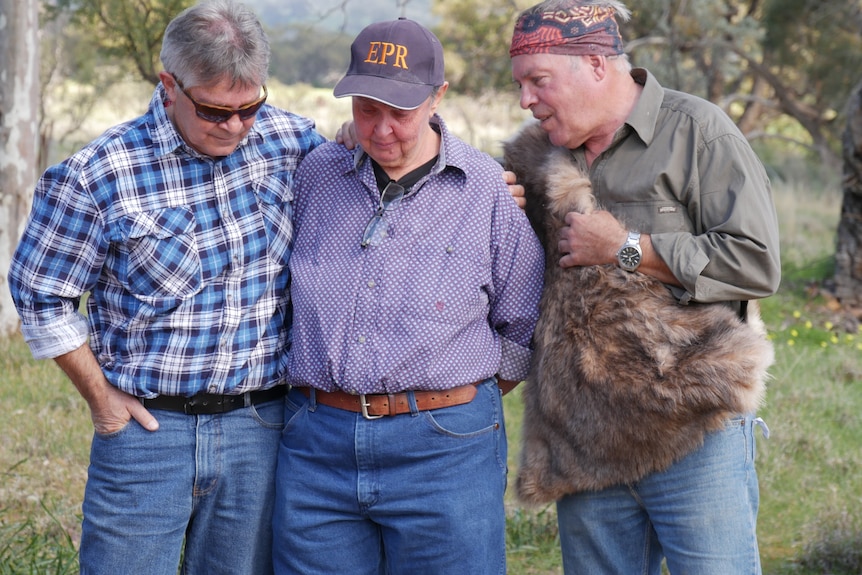 Two indigenous elders embrace a non-indigenous woman, all three are quite emotional