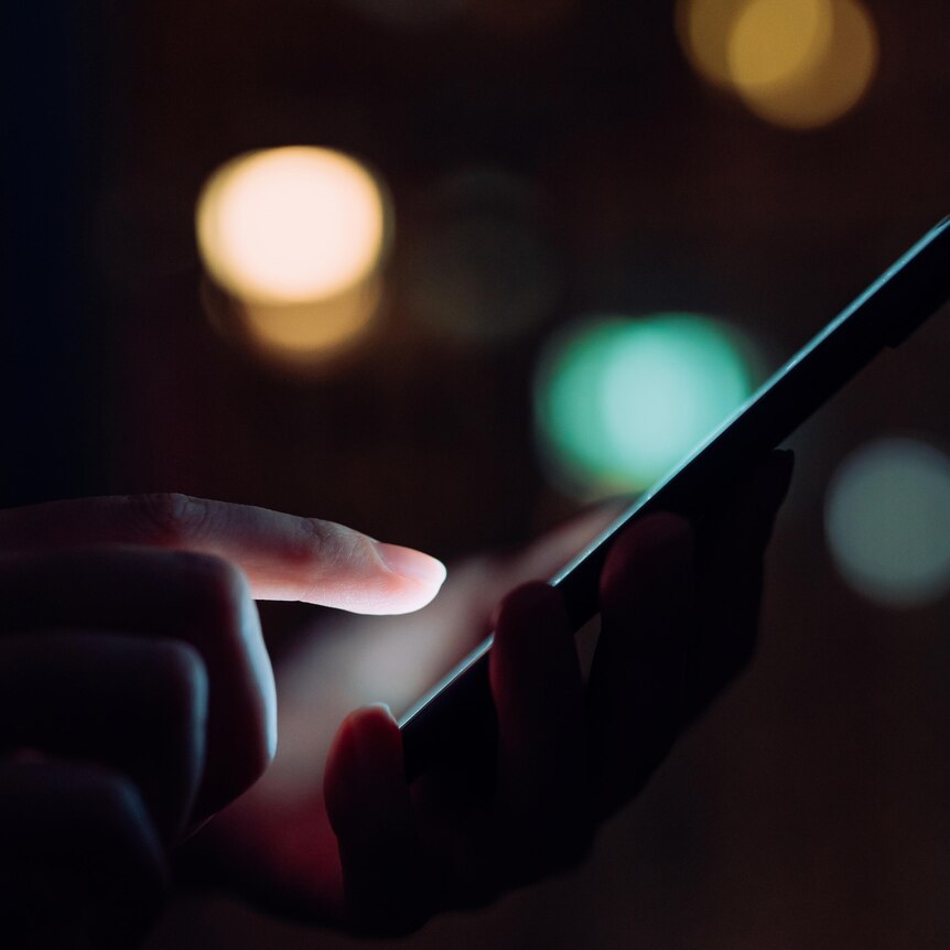 Closeup of a woman's hand using smartphone in the dark against a backdrop of city lights