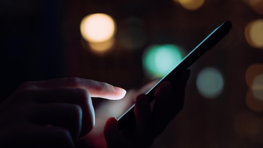 Closeup of a woman's hand using smartphone in the dark against a backdrop of city lights
