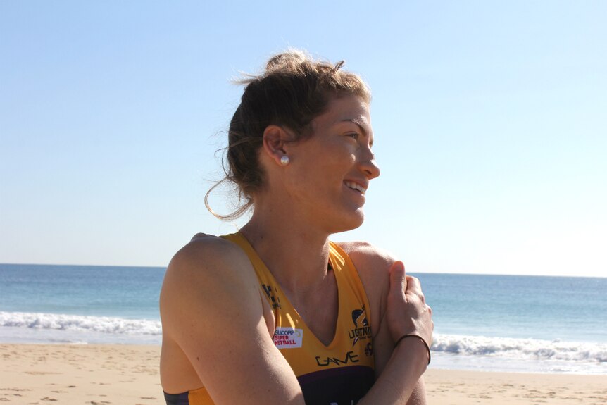 Professional netballer standing at the beach smiling, looking away from the camera.