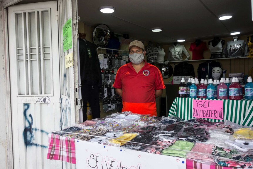 A man in a red shirt wears a face mask as he sells clothes and anti-bacterial sanitizer gel.