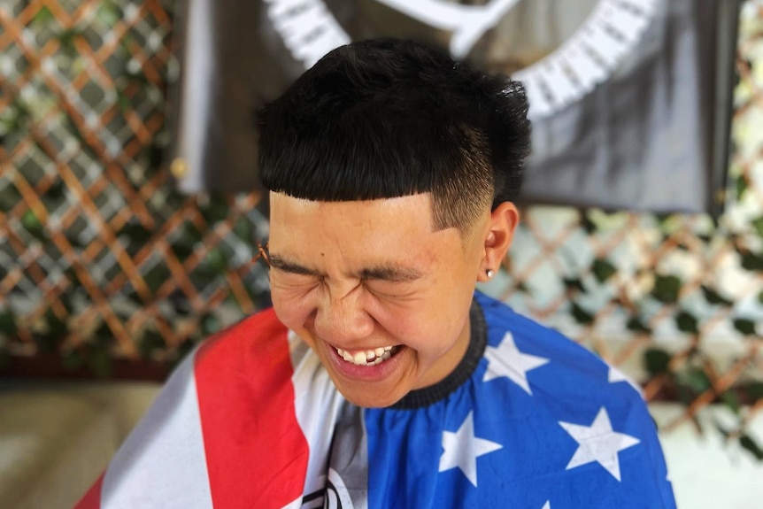 A young man laughs while getting a haircut