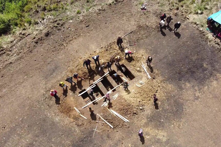 A top view of five rectangles dug into the ground with people surrounding them