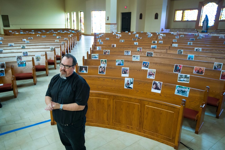 A Catholic priest stands in an empty church with images of parishioners fastened on to rows of pews.