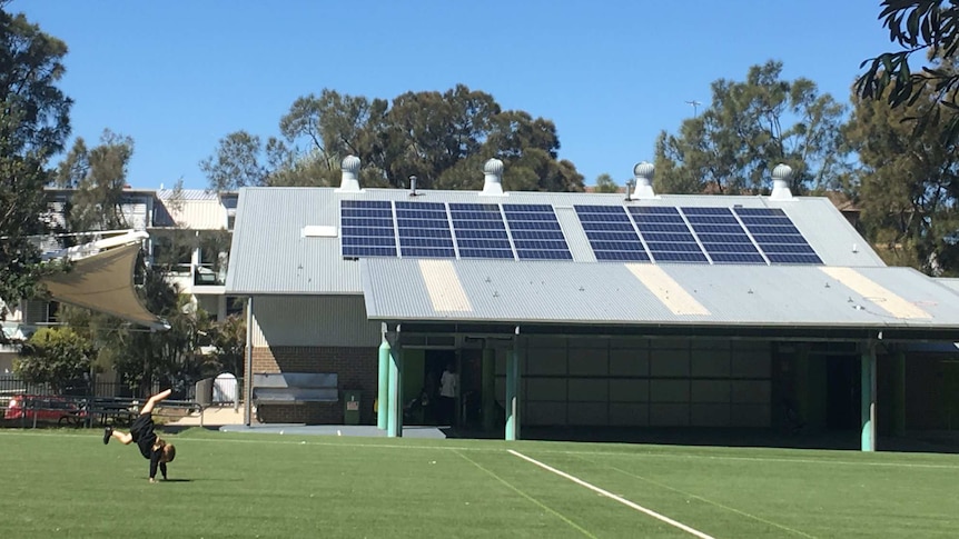 A student does a handstand in front of a school building with solar panels