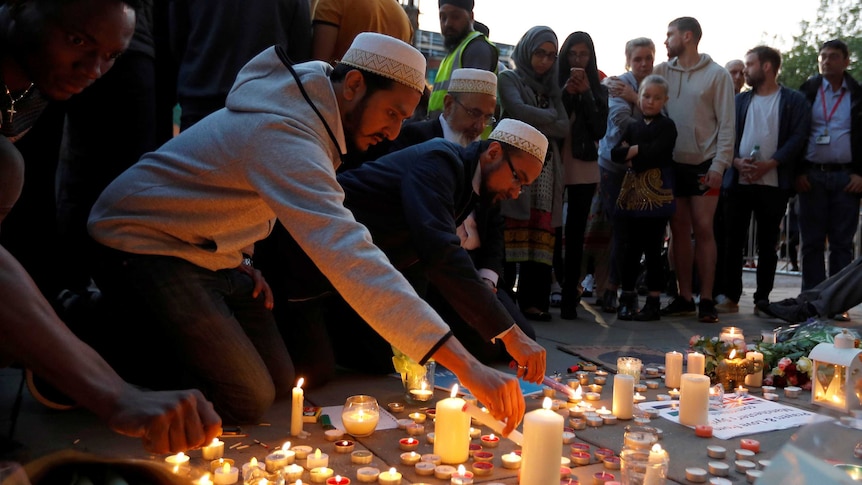 Islamic men wearing traditional headwear light tea candles on the concrete at the vigil in central Manchester