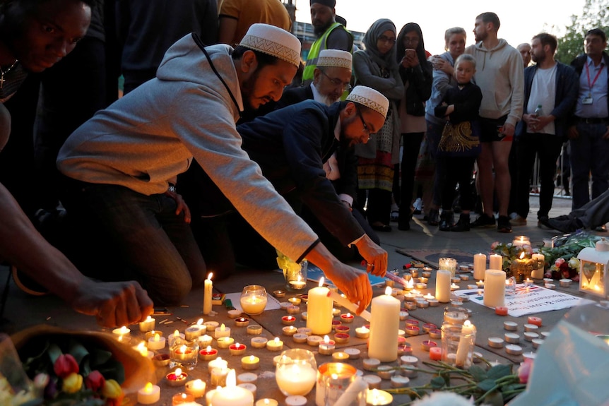 Islamic men wearing traditional headwear light tea candles on the concrete at the vigil in central Manchester