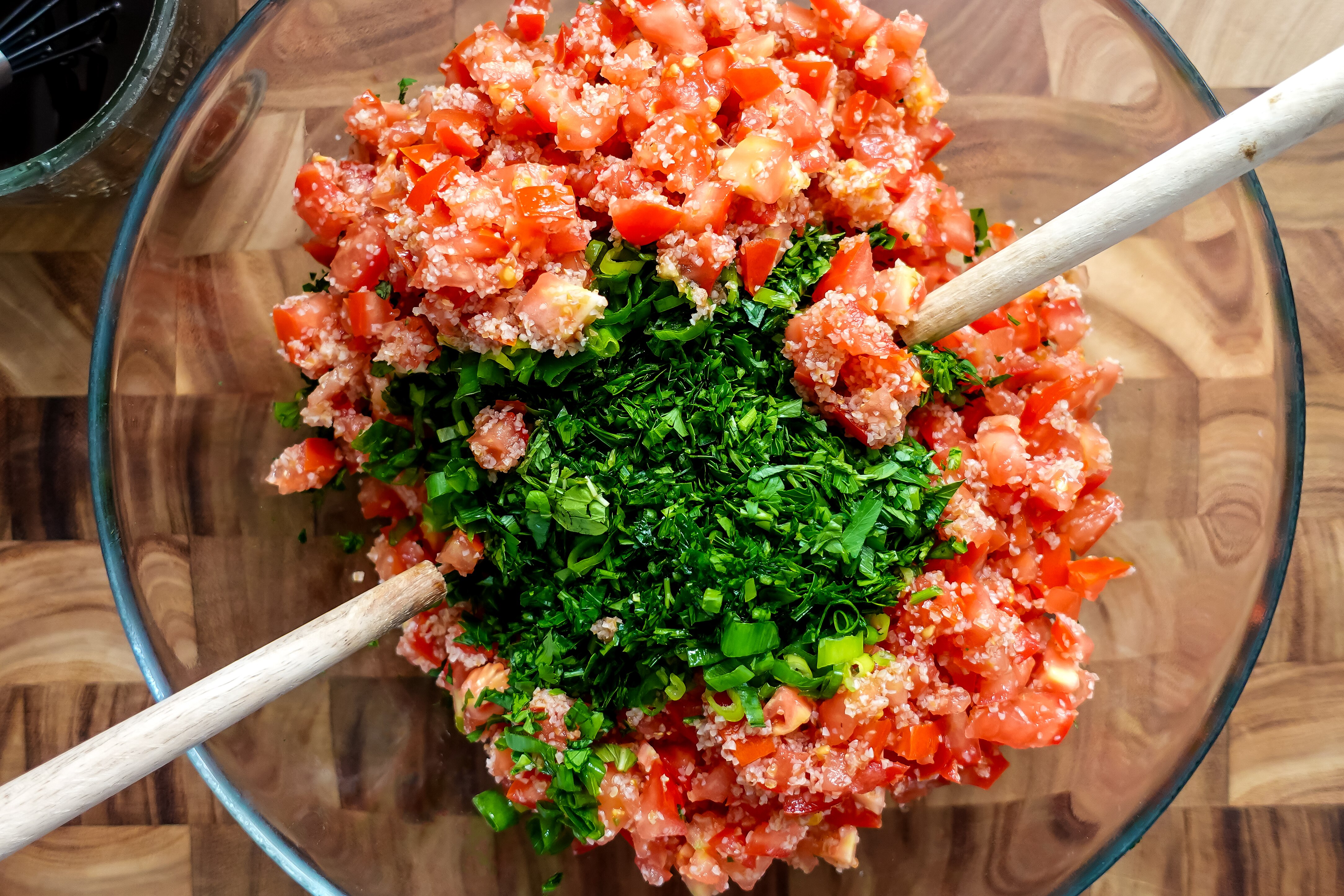 Fresh chopped herbs and spring onion are added to a bowl of tomato and bulghur to make tabouli.