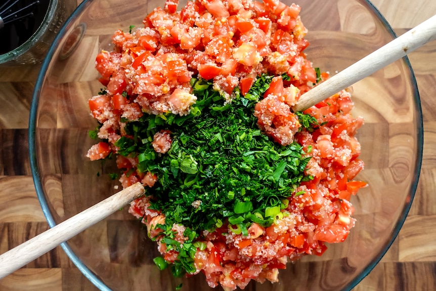 Fresh chopped herbs and spring onion are added to a bowl of tomato and bulghur to make tabouli.