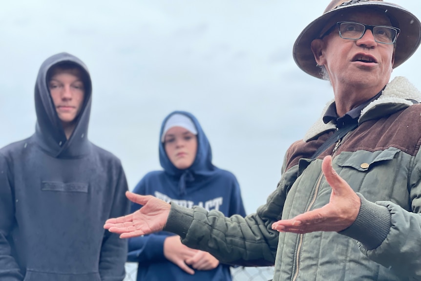 Uncle Gavi Duncan is motioning with hands as he talks, in front of two teenagers wearing hoodies on a cloudy day.