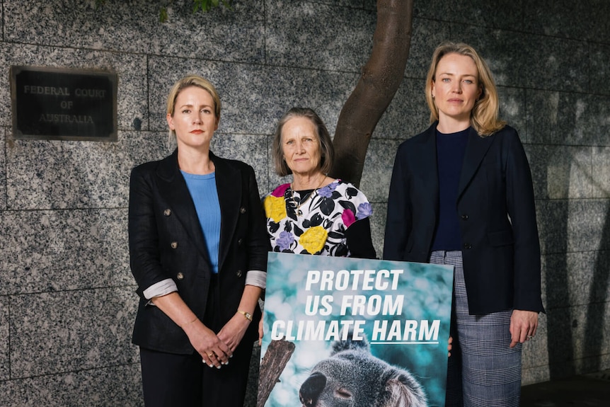 Three women standing behind a poster saying 'protect us from climate harm'.