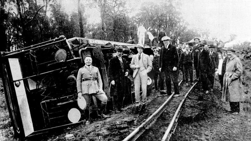 A b&w photo of the Prince of Wales and his entourage standing in front of a de-railed train
