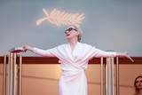 Meryl Streep in a white dress and sunglasses, arms outstretched, head thrown back, beneath the Cannes symbol