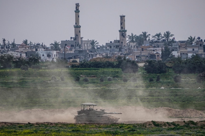 A lone tank operates on dusty field with city skyline behind