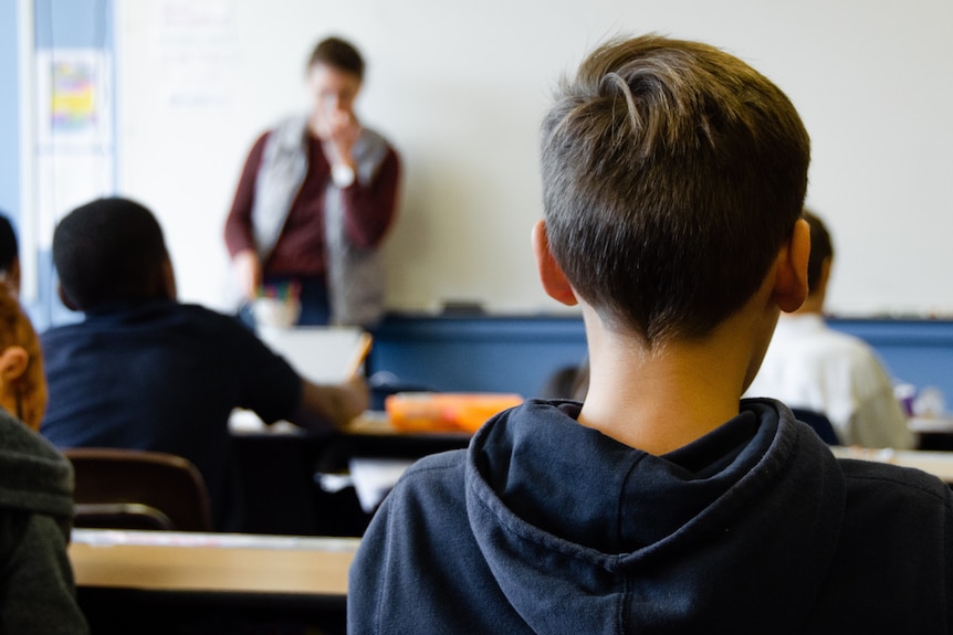 Students in a classroom with male teacher in background.