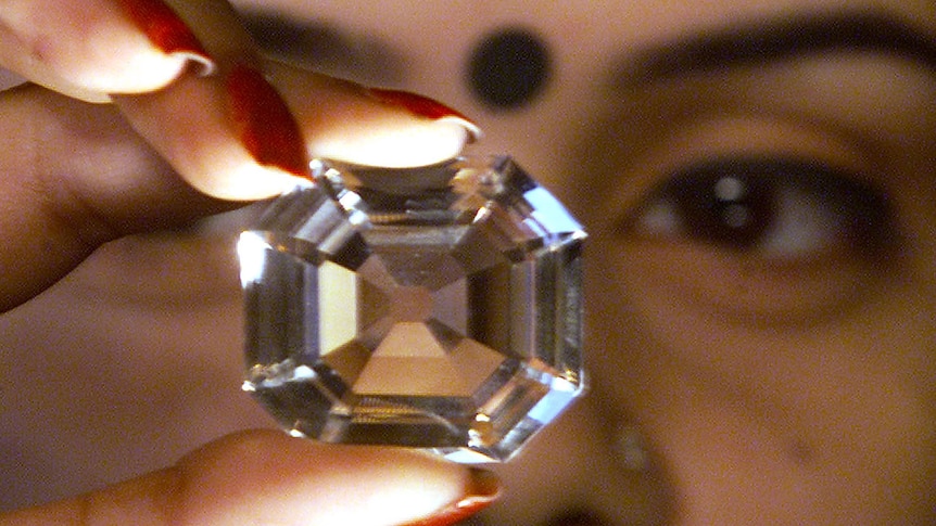 A woman with red nails and a bindi on her face holds up a giant diamond