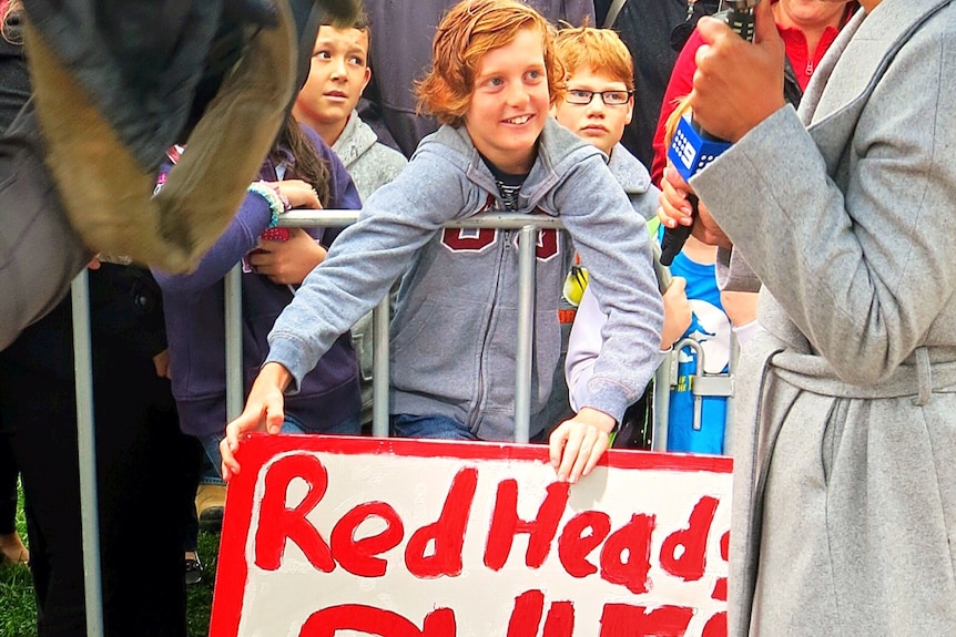 A child wielding a 'Red Heads Rule' sign waits to see Prince Harry in Canberra.