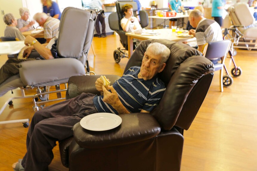 A Lyndoch Living resident sitting on a chair in the dining room eating a soft textured sausage.