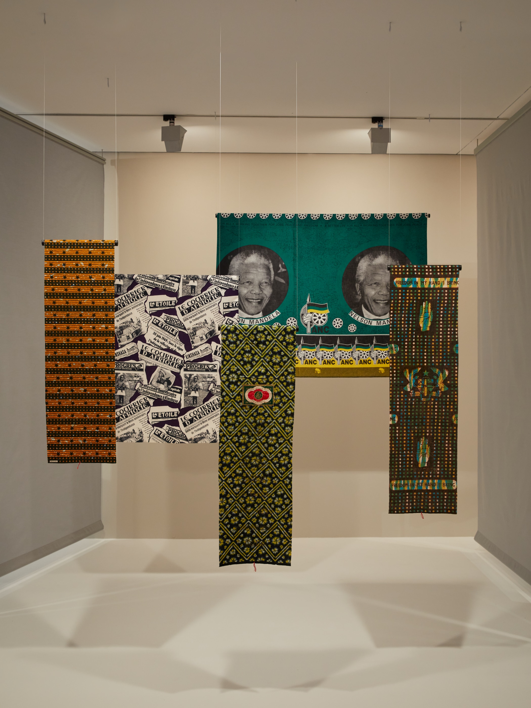 Five pieces of commemorate cloth hung up, one with Nelson Mandela's face twice against a green background.