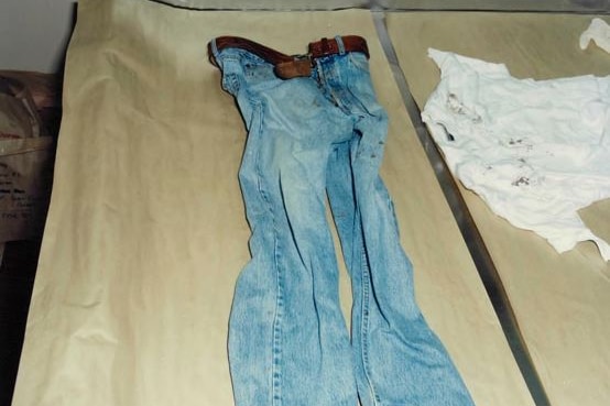 Crispin Dye's bloodstained jeans and white shirt on a table. Red marks can be seen on the leg of the pants and on top of shirt