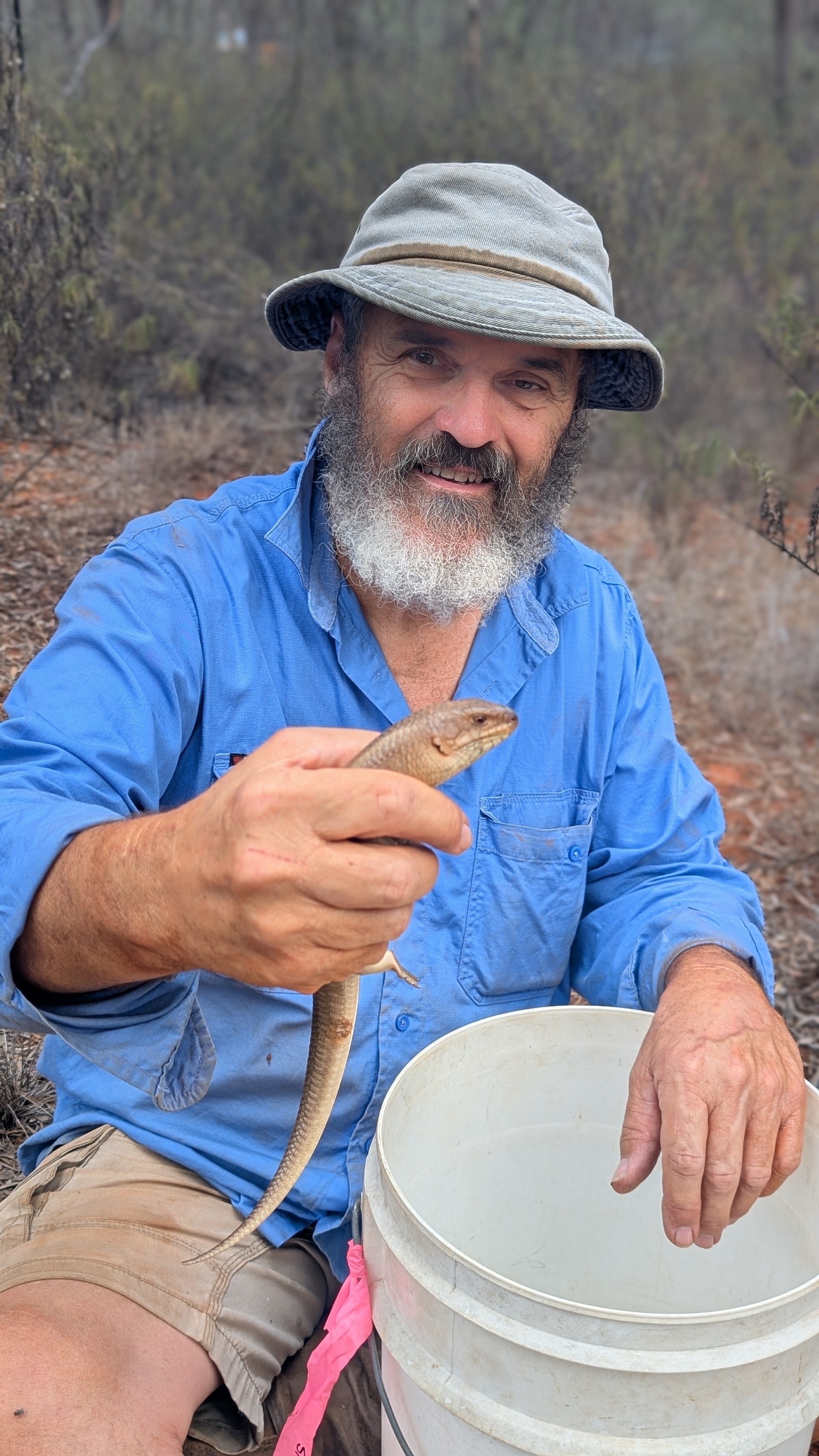 a man in bucket hat and blue shirt holds a skink in front of him