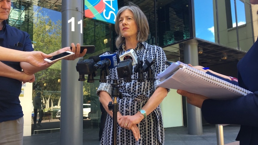 A woman speaks into microphones in front of SA Health building