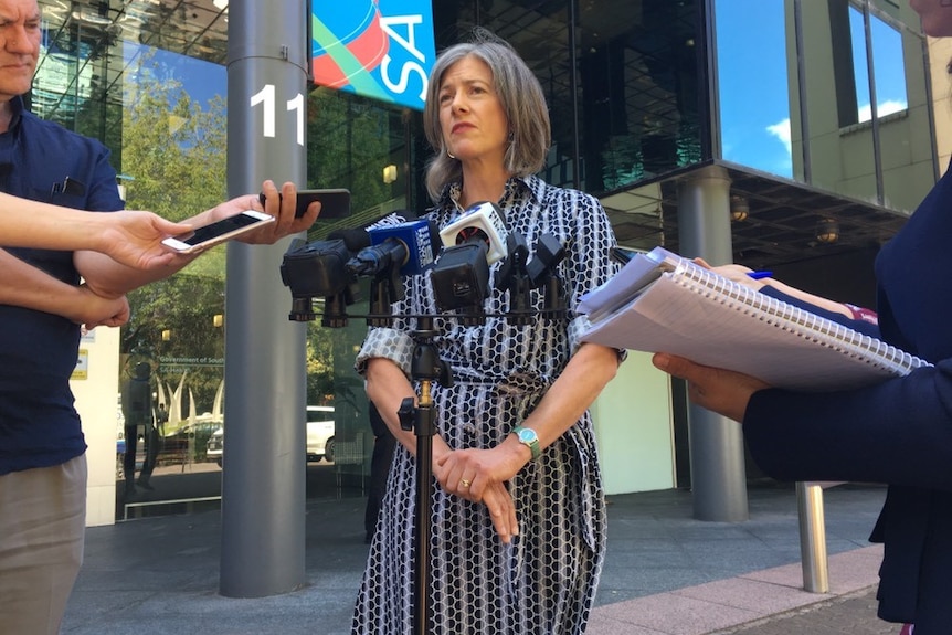 A woman speaks into microphones in front of SA Health building
