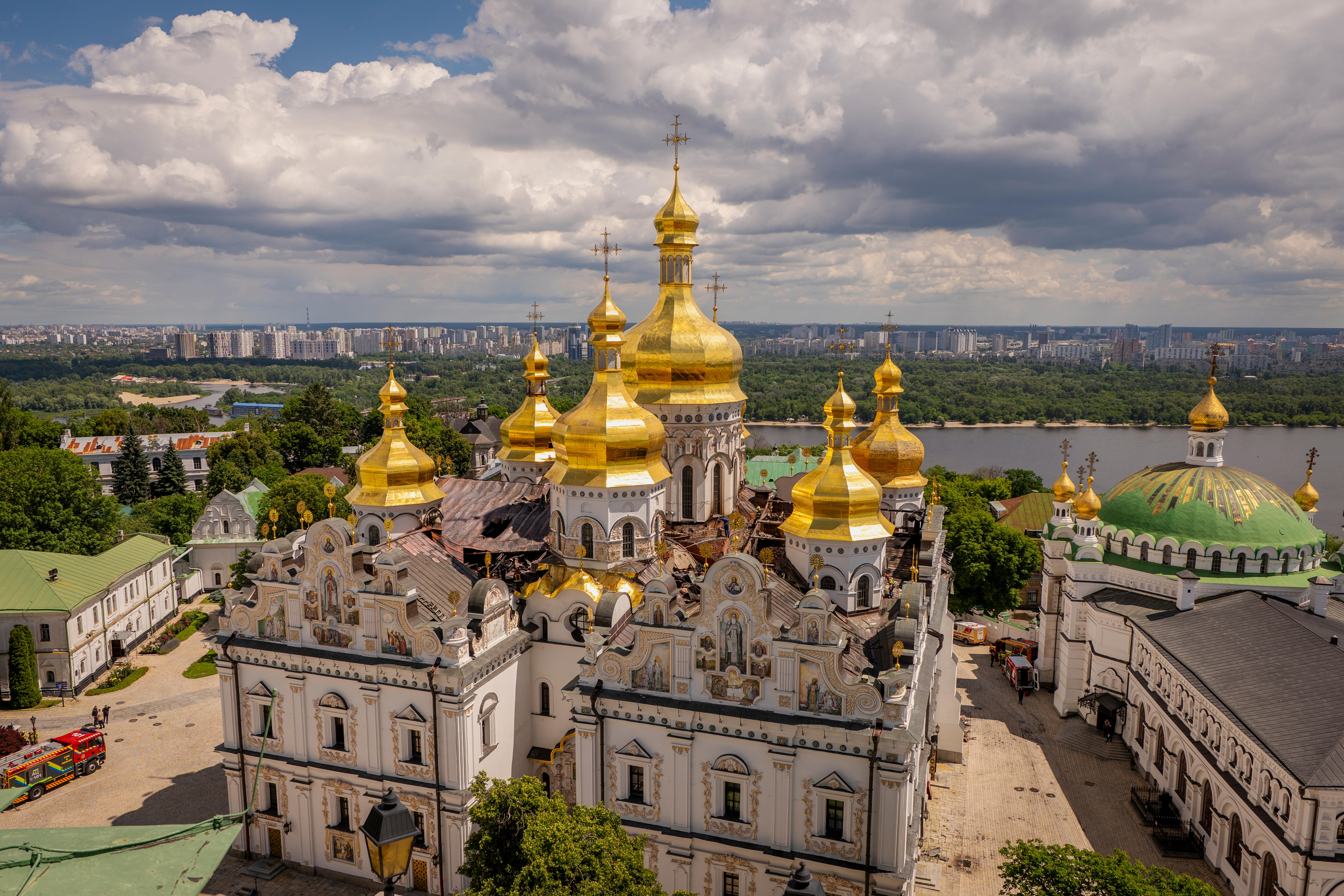 A cathedral with several golden domes in the sun sitting next to a river. 