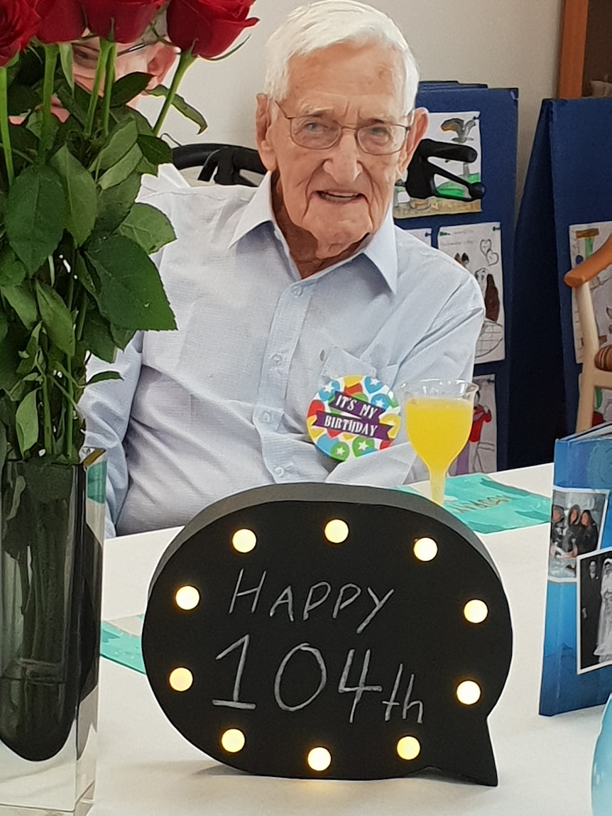 Fred Power sits in front of a sign saying 'happy 104th' with a drink of juice.