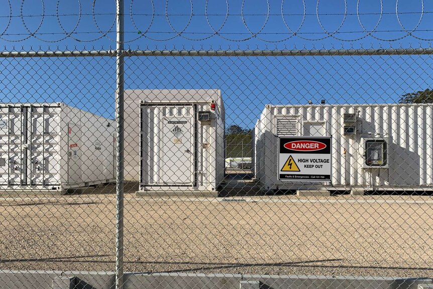 Large batteries behind a barbed wire fence, with a sign saying "Danger: High voltage, keep out".