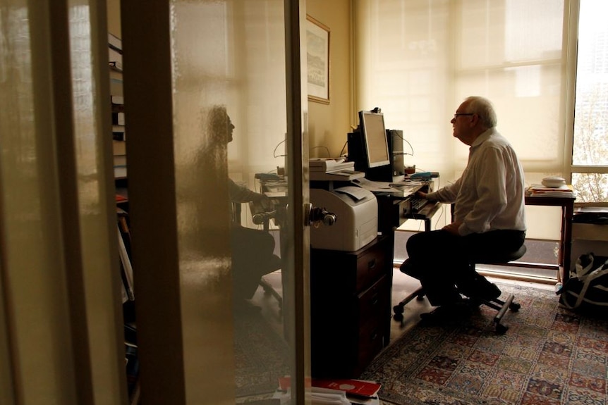 A photo taken from the door looking in to Dr Stephen Duckett's office. He works at a computer on a desk.