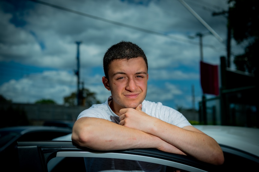 Ethan smiles and looks at the camera as he leans on the car door.