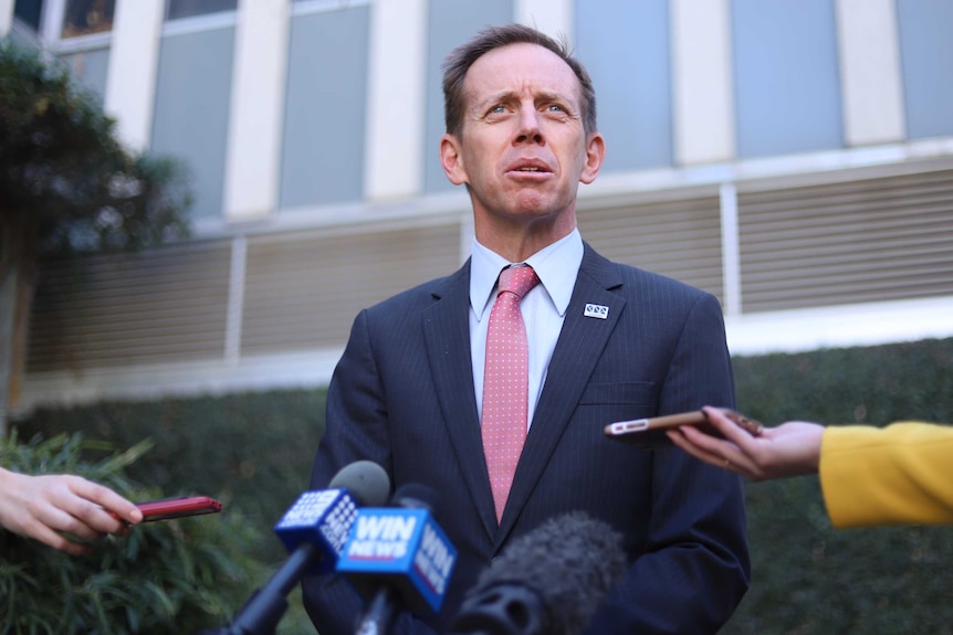 Shane Rattenbury speaks behind a host of media microphones.