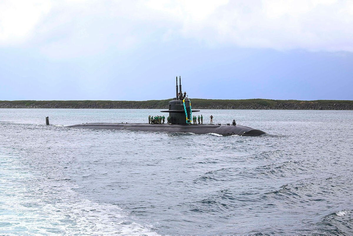 A submarine makes its way into port with sailors standing on its deck