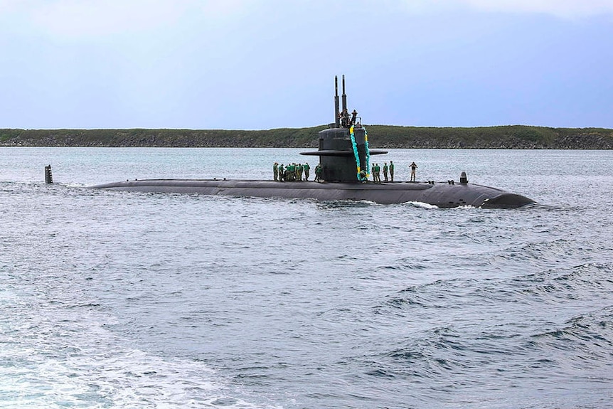 A submarine makes its way into port with sailors standing on its deck