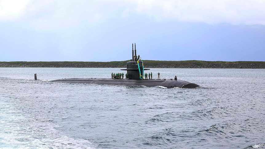 A submarine makes its way into port with sailors standing on its deck