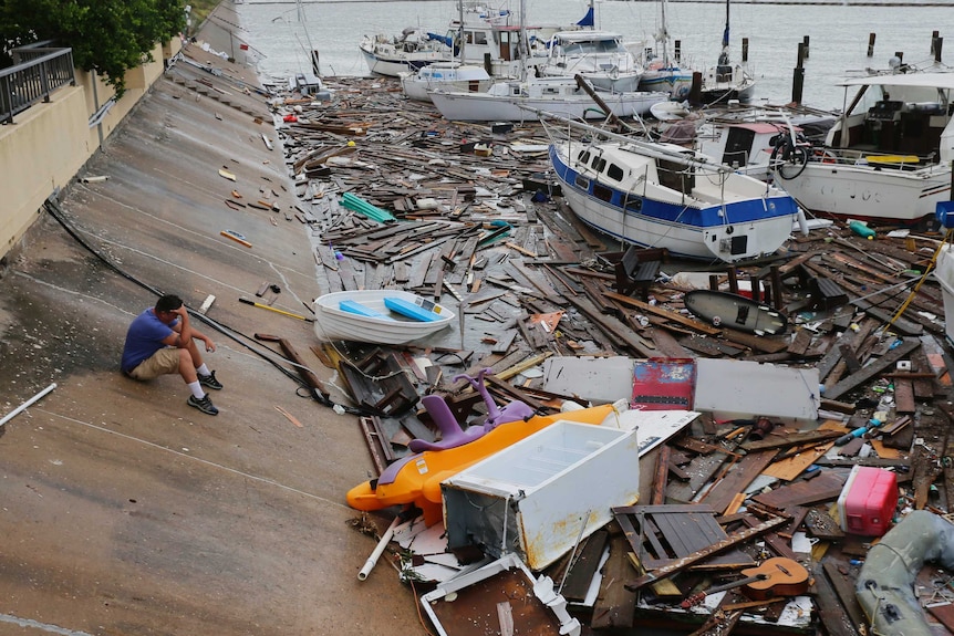 A man sits and looks at debris that is surrounding boats in the ocean