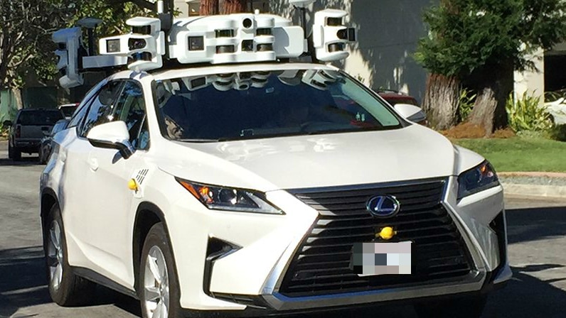 A modern white car has a large contraption, containing what look like multiple cameras and sensors, on its roof