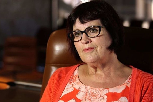A dark-haired, bespectacled woman wearing a bright top.