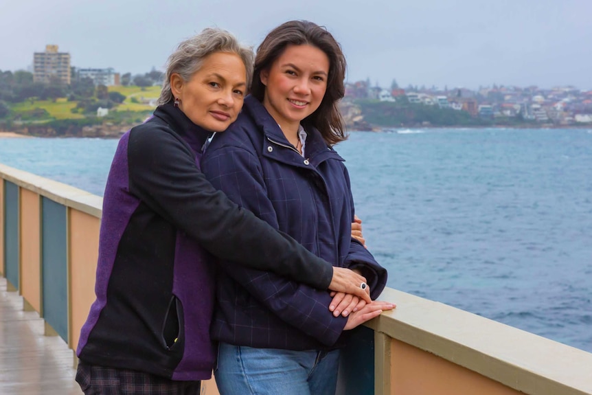 A woman and her adult daughter stand beside the water