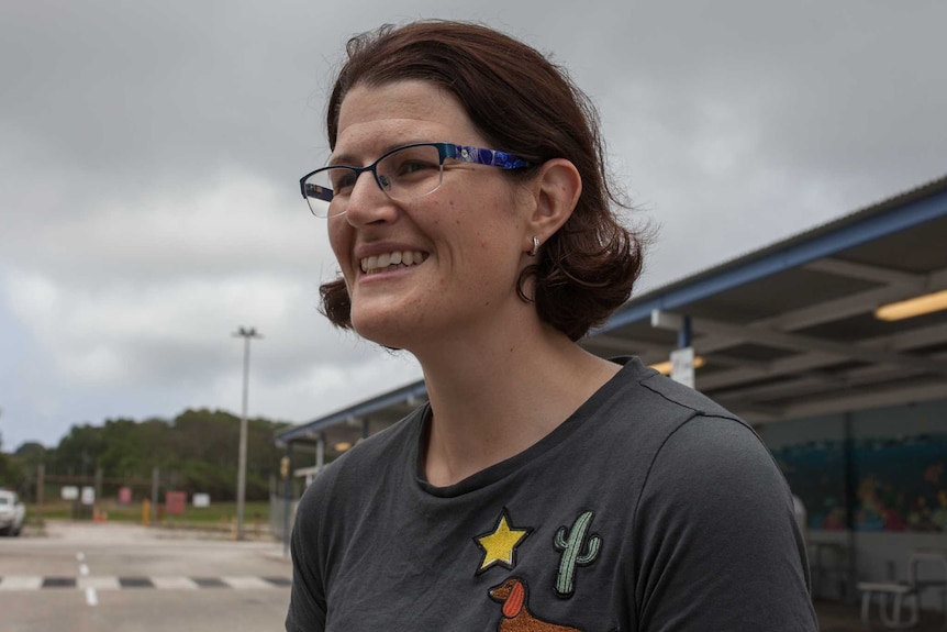 A woman outside a small airport wearing a grey t-shirt and glasses.