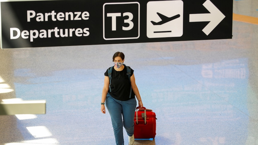 A woman pulls a red suitcase through an empty terminal.