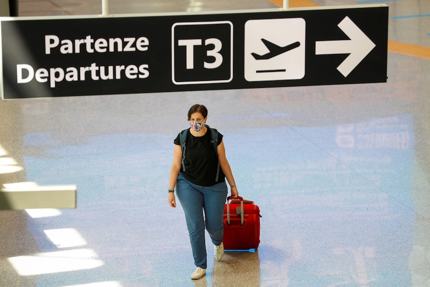 A woman pulls a red suitcase through an empty terminal.