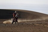 Dakar Rally rider navigates the sandy dunes during the rally, leaving a dusty trail behind him.