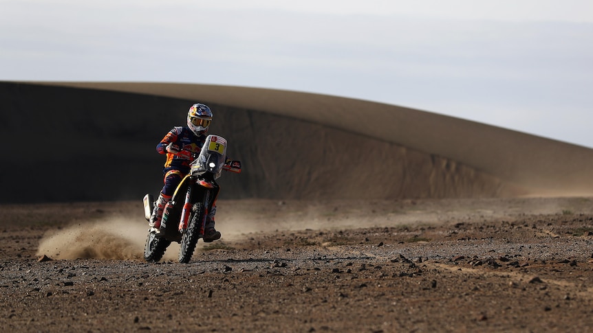 Dakar Rally rider navigates the sandy dunes during the rally, leaving a dusty trail behind him.