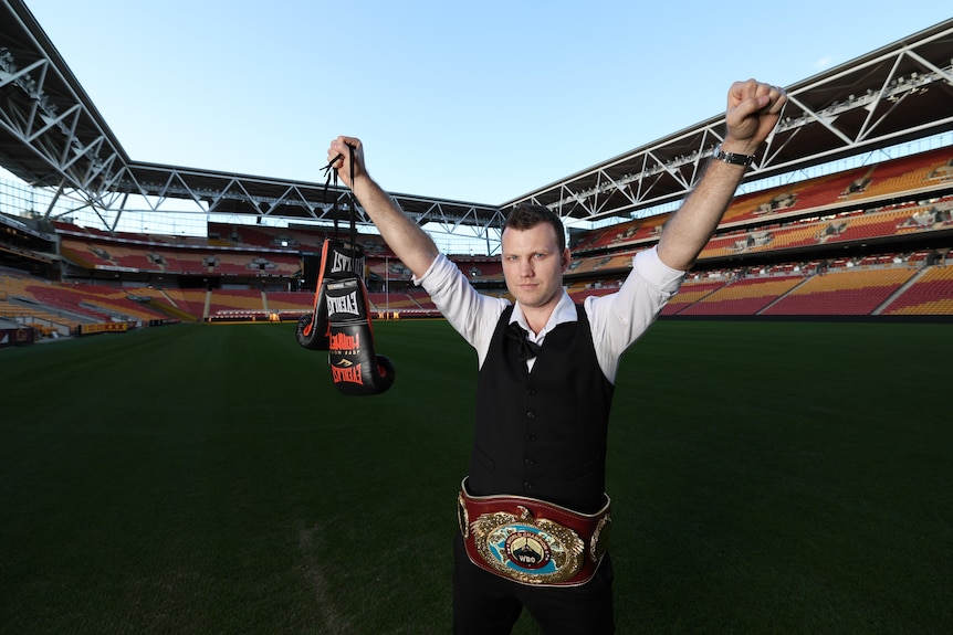 jeff stands in suncorp stadium holding boxing gloves with his hands up in the air 