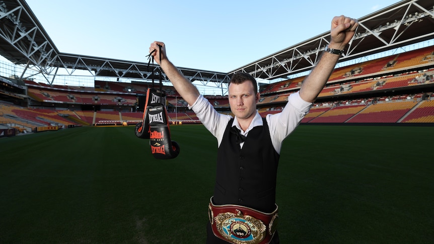 jeff stands in suncorp stadium holding boxing gloves with his hands up in the air 